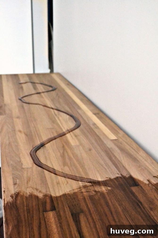 Applying Howard Butcher Block Conditioner to the walnut surface of the new kitchen bar, highlighting the immediate color enhancement.