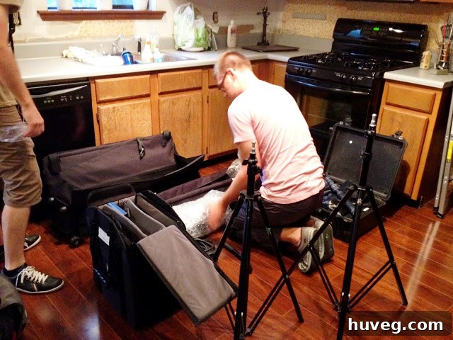 Professional film crew setting up sophisticated camera and lighting equipment in a cozy home kitchen for a shoot, showcasing unexpected guests and a busy week.
