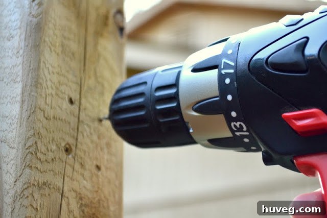 A hand holding a power drill, precisely drilling a pilot hole into the wooden gate for the new latch installation