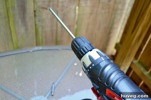 A close-up shot of a hand operating a power drill to install the other side of the gate latch, demonstrating the use of both hands for stability