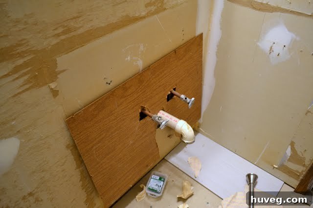Unfinished, messy wall area behind the toilet, showing rough construction and uneven surfaces.
