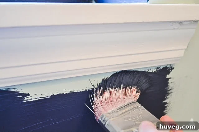 Close-up of a brush applying a clean, straight paint line near a window without tape