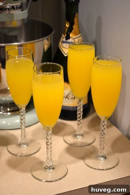 Close-up of bright orange mimosas in flutes, appearing to glow with festive cheer.