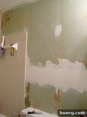 Bathroom wall after initial wallpaper removal, showing imperfections and old adhesive