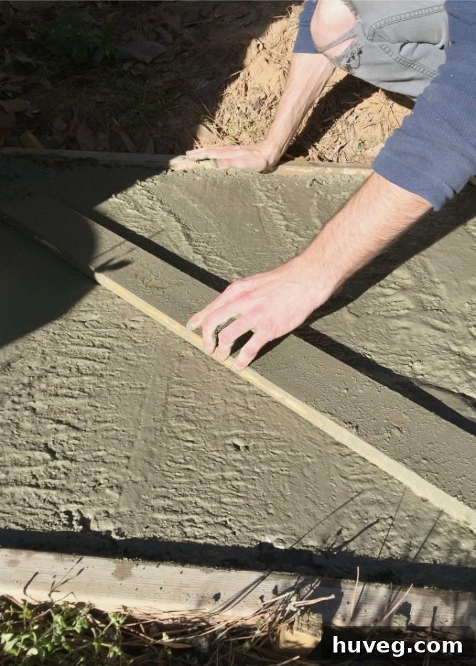 Leveling and smoothing the freshly poured concrete slab with a 2x4