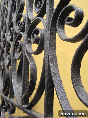 Intricate black wrought iron balcony detail against a creamy stucco wall, a classic New Orleans architectural texture suitable for unique home decor.