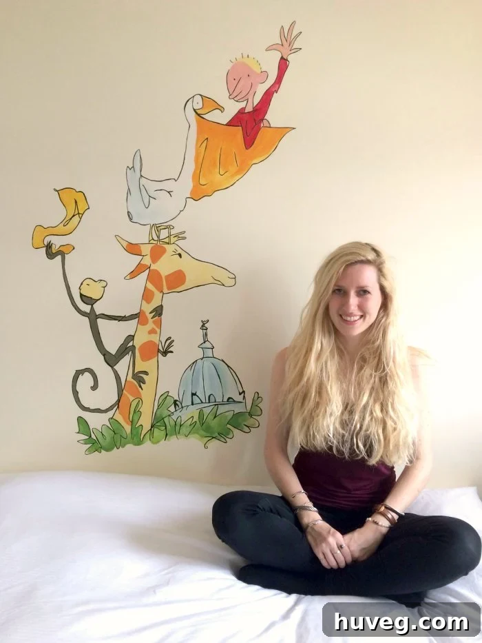 Ruth Stolerman proudly standing next to her vibrant, hand-painted children's bedroom mural, showcasing her artistic talent and the joy of custom wall art.