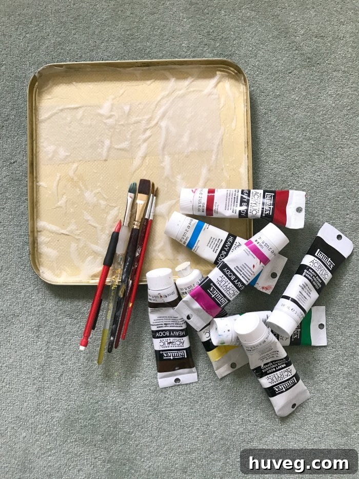An organized artist's palette with various acrylic paints, brushes, and a water glass, ready for a wall mural project.