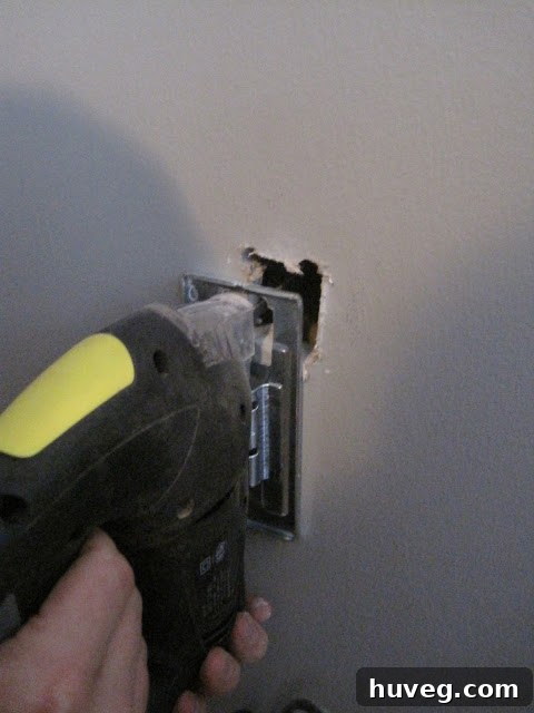 Jigsaw cutting the second hole in the drywall for wire exit