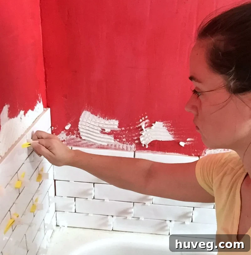 Tiling a bathtub shower surround with white subway tiles during bathroom renovation