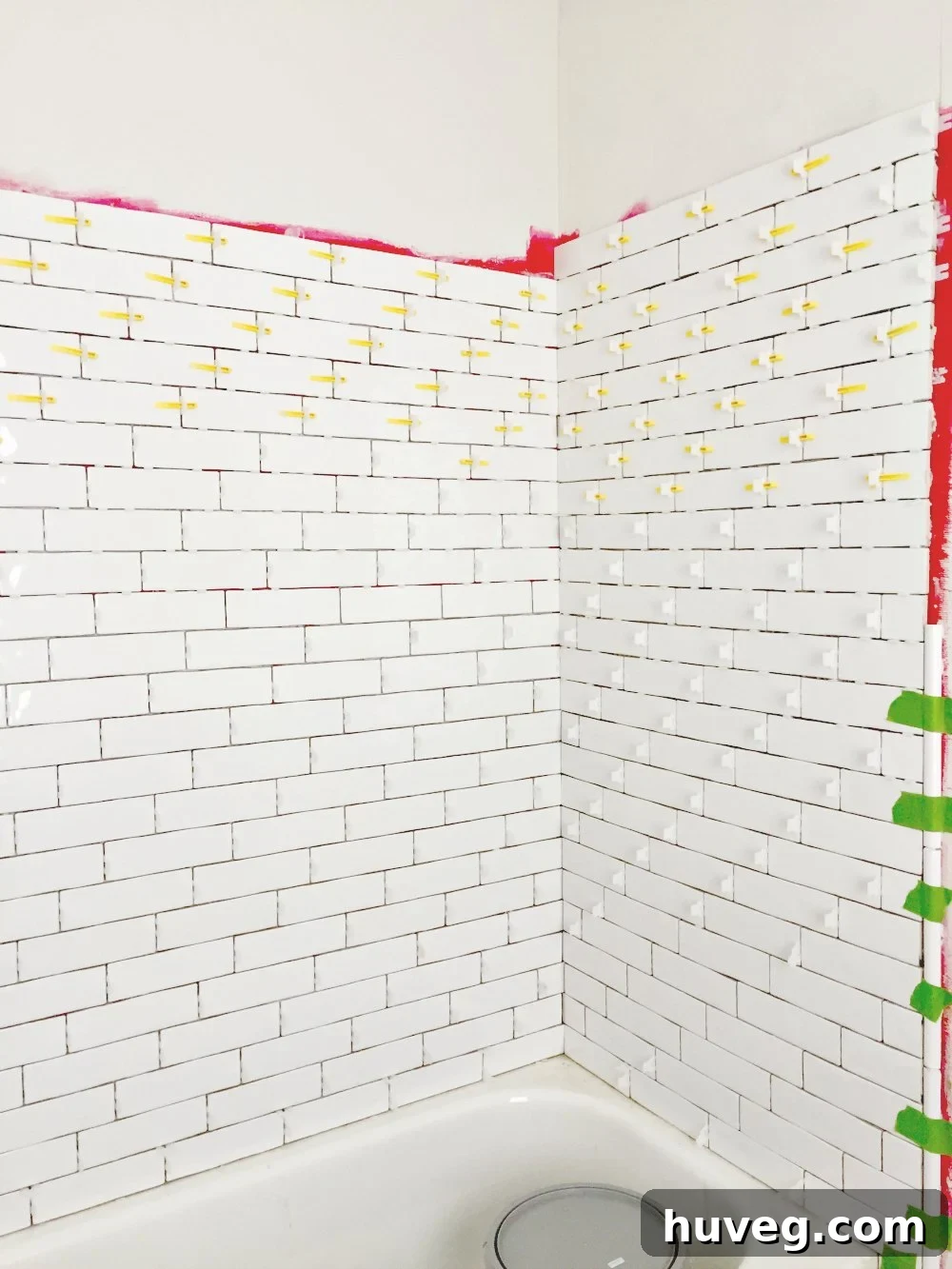 Tiling master bathroom tub surround with long white subway tile, showing waterproofing and tiling progress