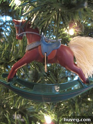 Close-up of a vintage Hallmark Christmas rocking horse ornament, dated 1983, with intricate details, hanging on a decorated Christmas tree amidst other ornaments.