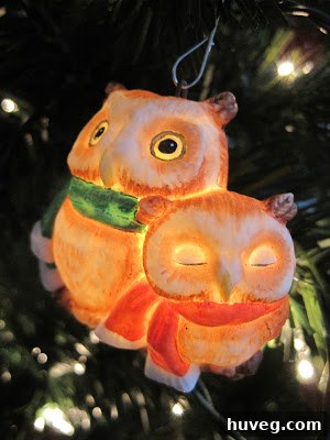 A pair of intricately designed owl Christmas ornaments that light up from within, showcasing delicate details and adding a warm glow to a decorated Christmas tree.