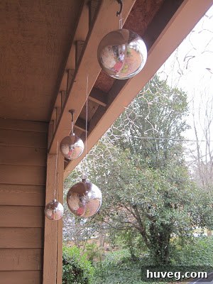 Large shatterproof ornaments in red and gold hues hanging from a front porch ceiling, creating a festive, cascading display.