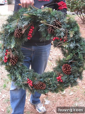 Large lit Christmas wreath temporarily held against a second-story window of a house, prior to permanent installation.
