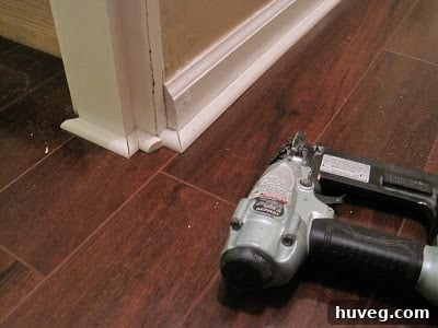 A close-up view of an air nailer positioned on newly installed shoe molding, ready for precise fastening, emphasizing the convenience and power of the tool.