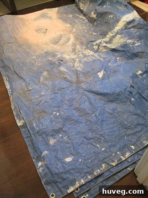Large blue plastic tarp spread on the floor directly beneath a ceiling water stain, demonstrating an emergency measure to collect drips.