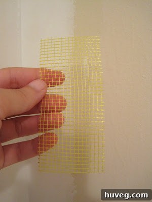 Hand holding a roll of drywall tape against a wall, showing proper application technique