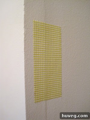 Fiberglass mesh drywall tape applied over a hole in a wall, ready for joint compound