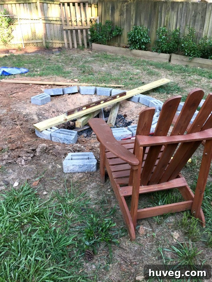 I dry-fitted the first layer of retaining wall stones to form the base of my backyard fire pit, confirming the desired size and shape next to my Adirondack chair.