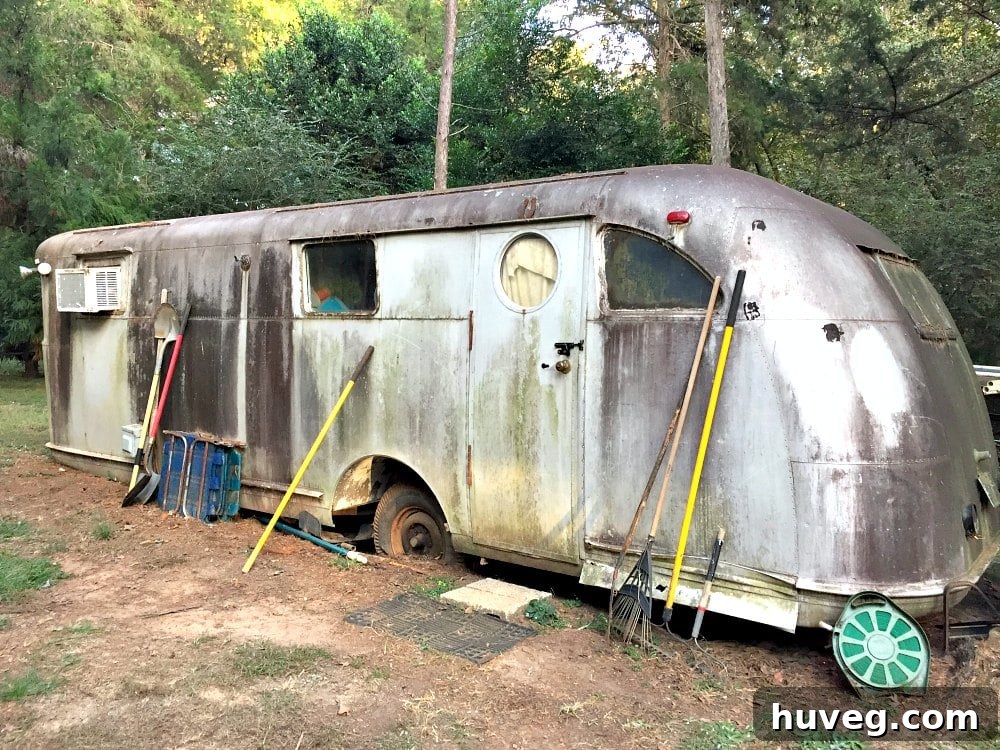 A weathered and neglected vintage travel trailer, a 1946 Spartan Manor, sitting in a field with flat tires, covered in grime and showing signs of decades of disuse.