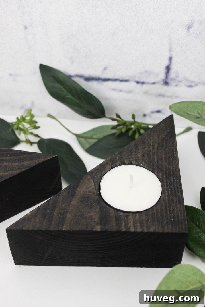Close-up of a dark, ebony-stained triangle tea light holder, highlighting its sleek lines and the soft glow of the candle.
