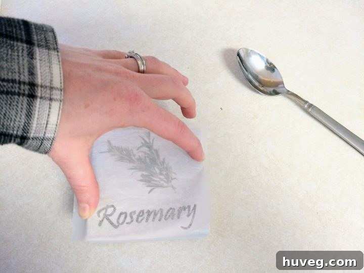 DIY enthusiast using a spoon to rub mirrored herb design from wax paper onto a wood block