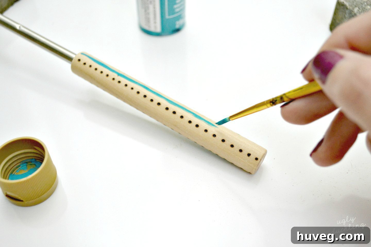 Applying craft paint freehand to create organic stripes and wrap-around patterns on the roasting sticks