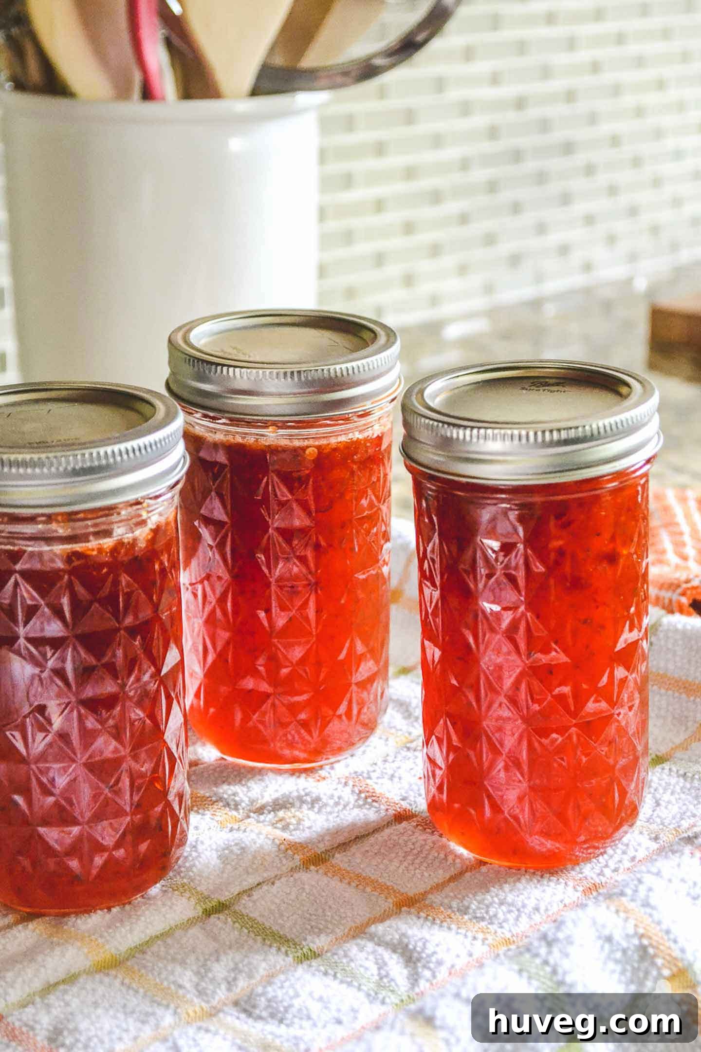 red pepper jelly in quilted mason jars with tiled background, a perfect sweet and spicy appetizer