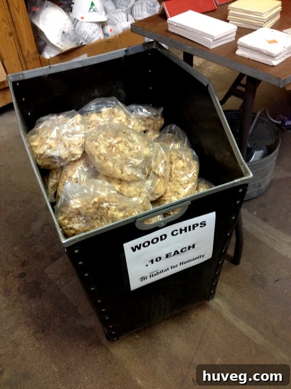 A large bin filled with various wood chips and scrap wood pieces, with stacks of tile and doors visible in the background at Habitat ReStore.