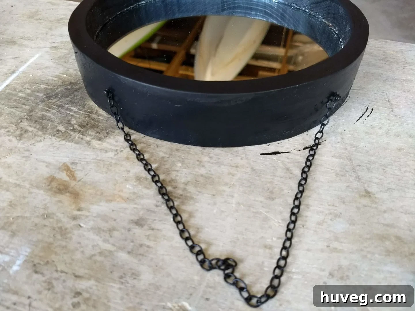 A small black chain attached to the top of the DIY round mirror frame for hanging, adding an industrial touch to the finished decor piece.
