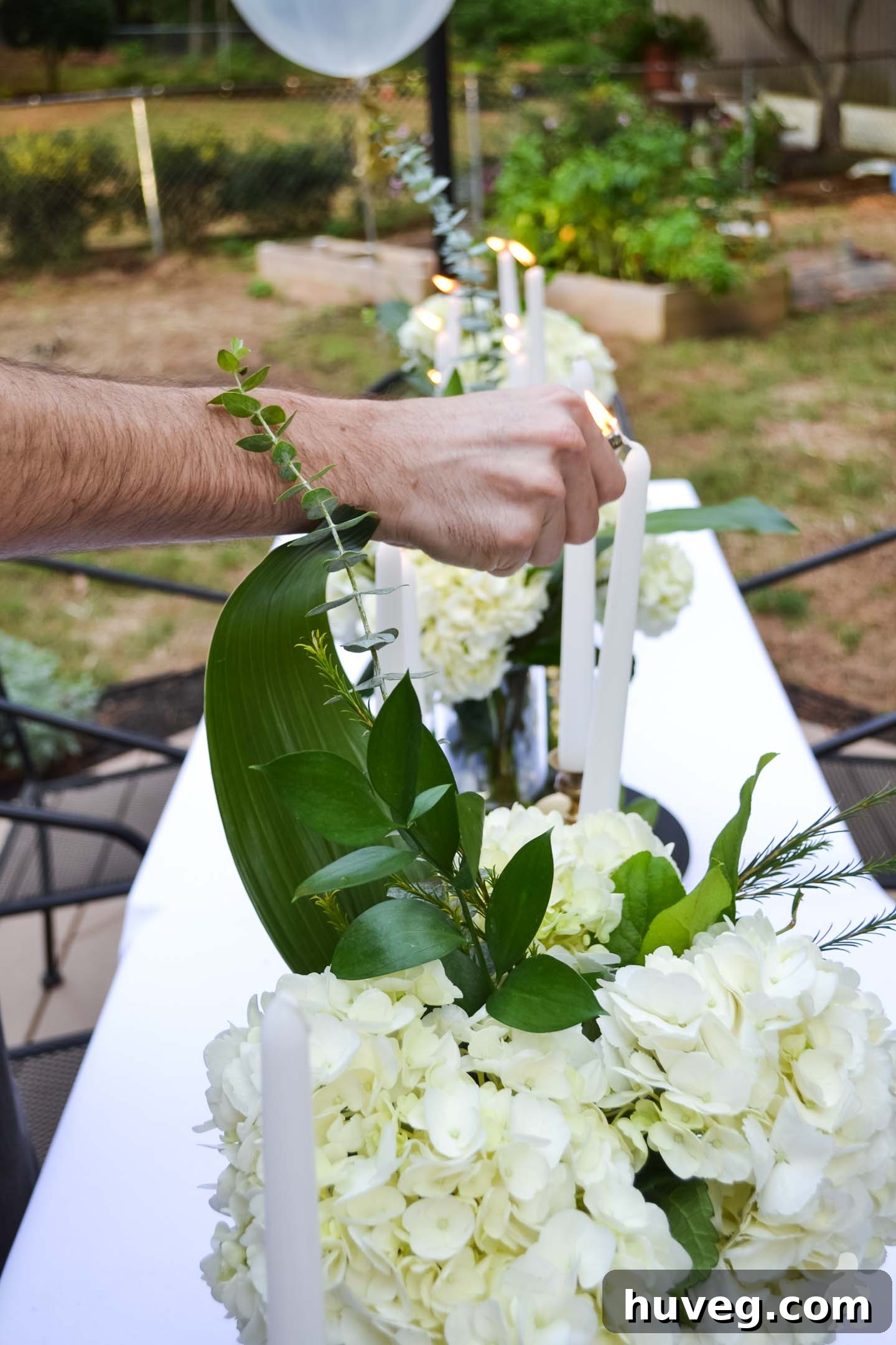 lighting candles with white hydrangea bouquets on long white table