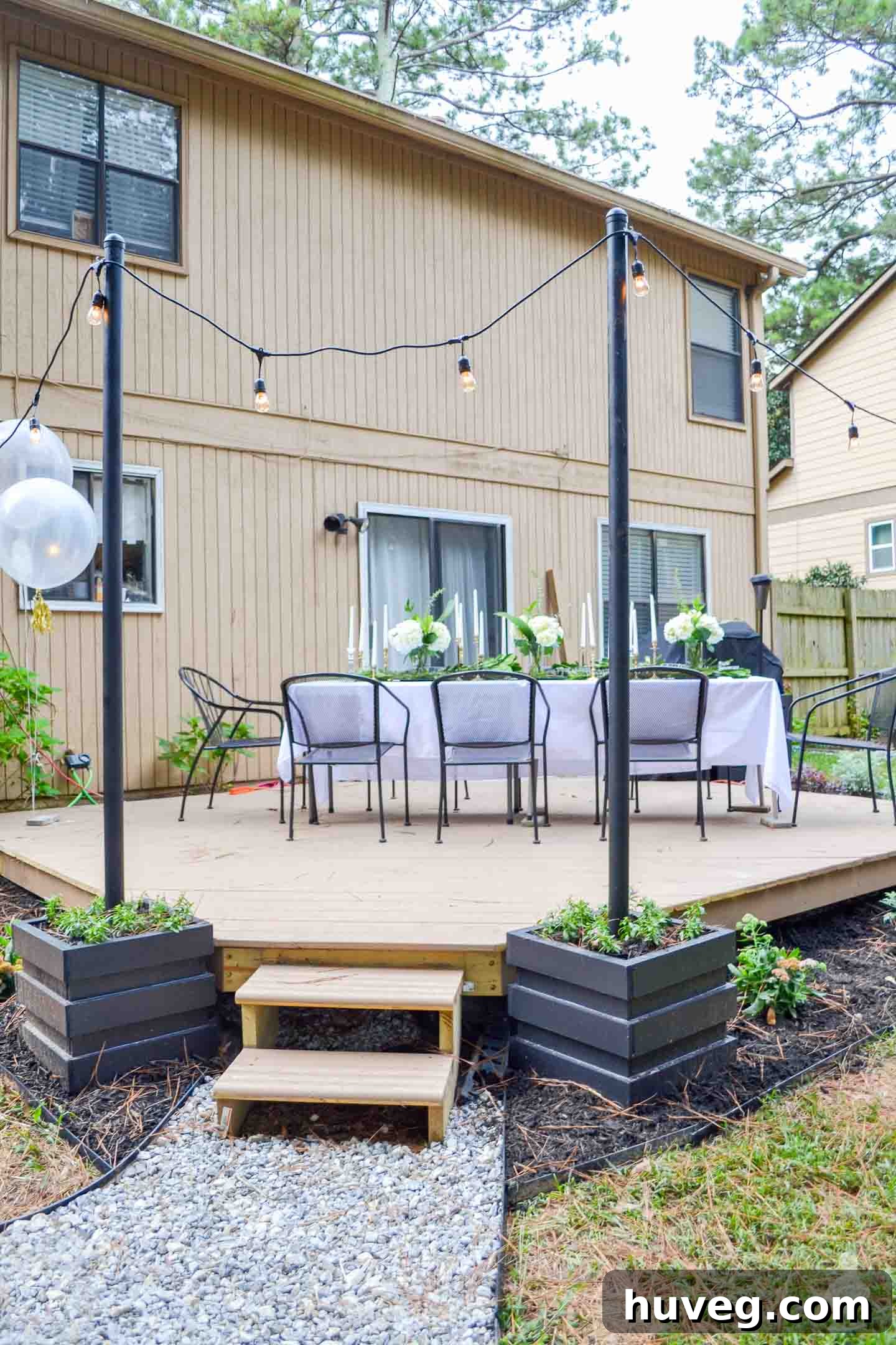 Outdoor Dining Table Setup with Black Light Poles and Hanging String Lights on Floating Deck