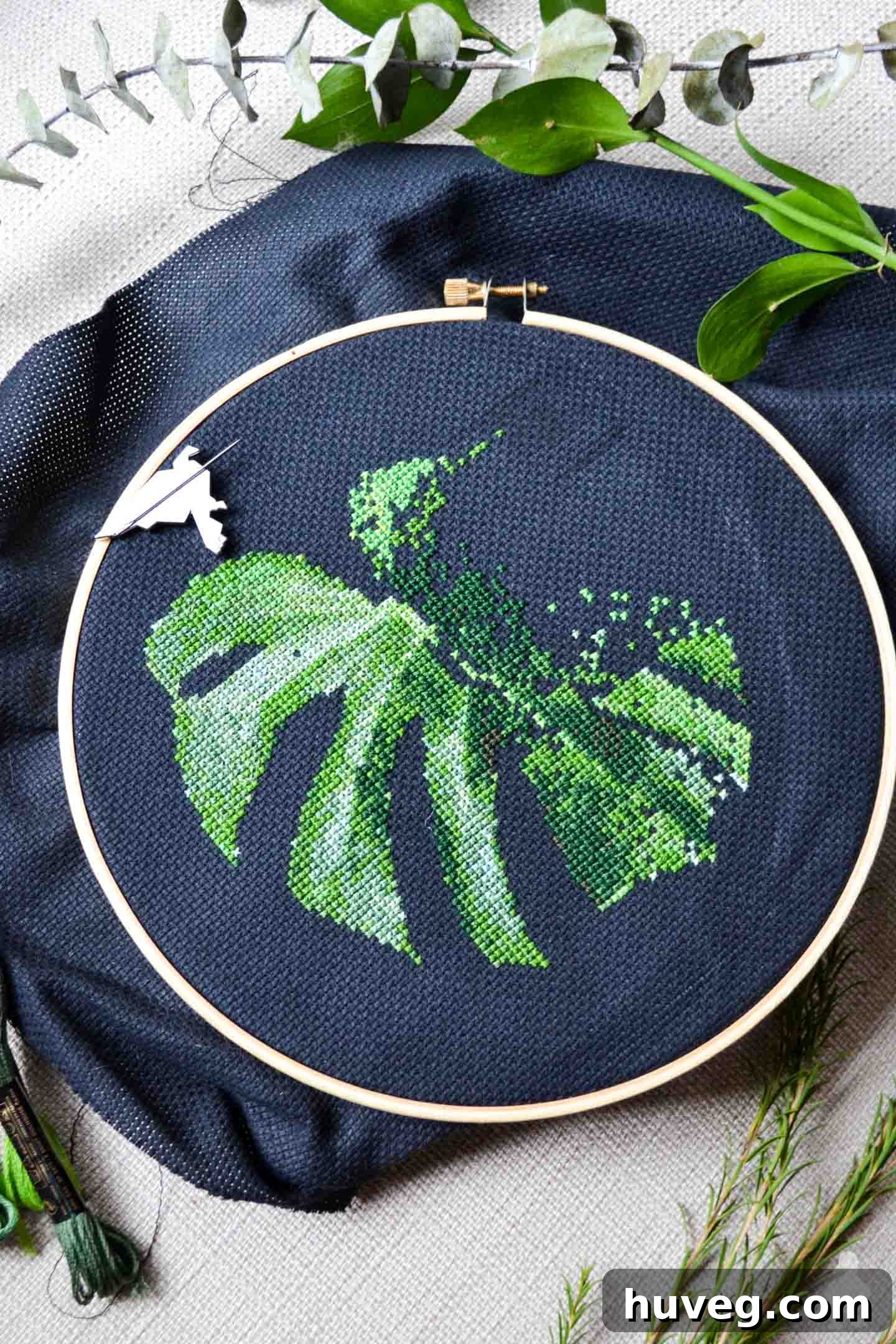 Work in progress of Monstera leaf cross stitch pattern on dark fabric, demonstrating the intricate stitching.