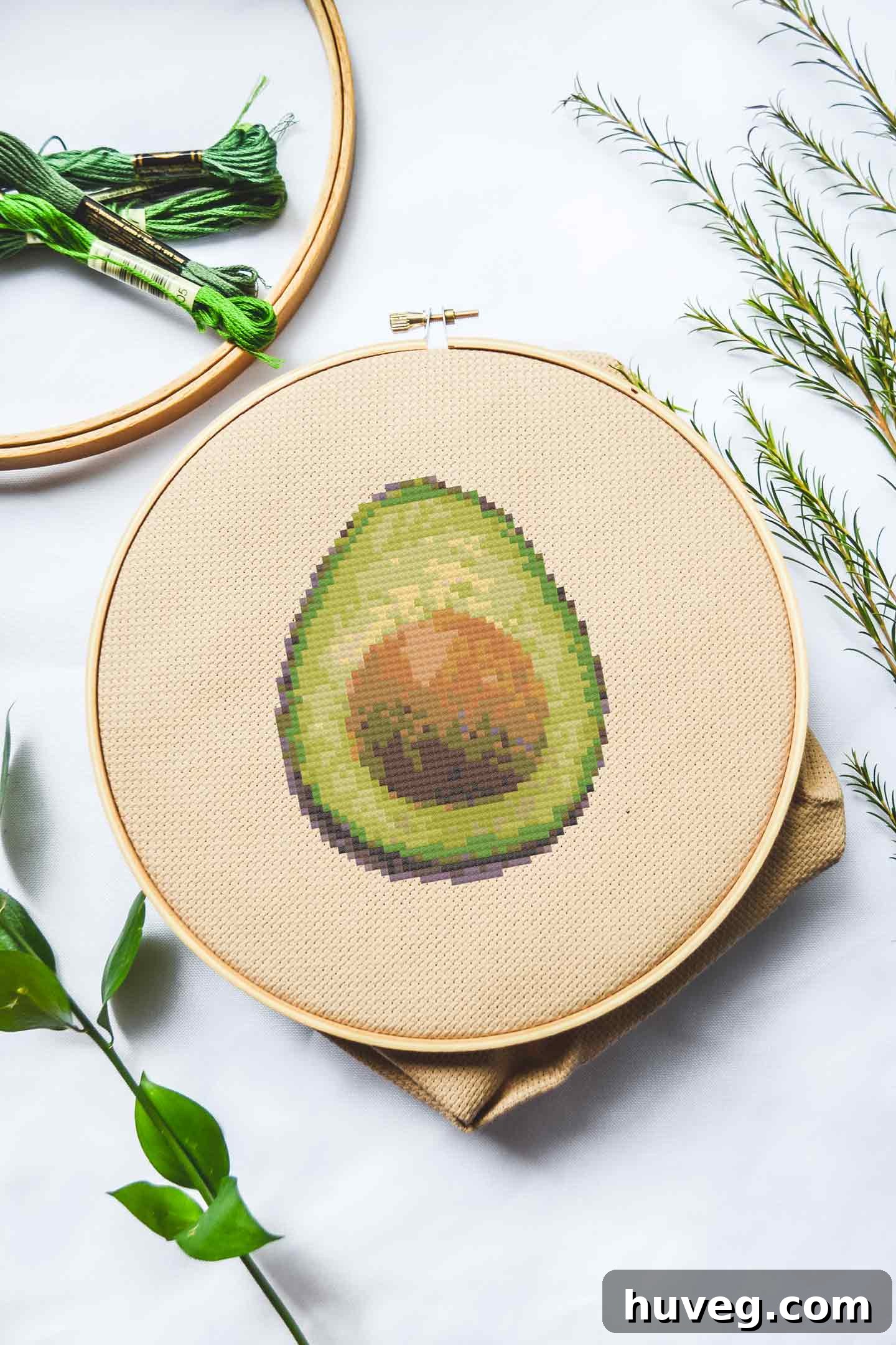 Vibrant green avocado cross stitch pattern on a light fabric, showcasing the pit and creamy flesh, perfect for food embroidery enthusiasts