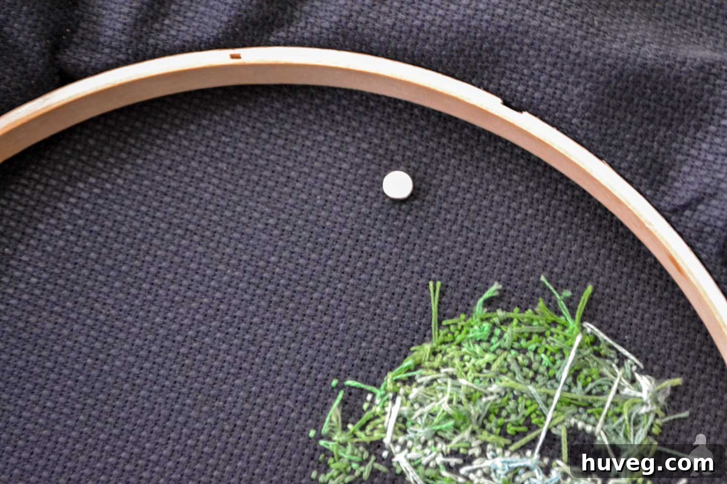 A tiny neodymium magnet placed on the back of black Aida cross stitch fabric, holding the needle minder in place.