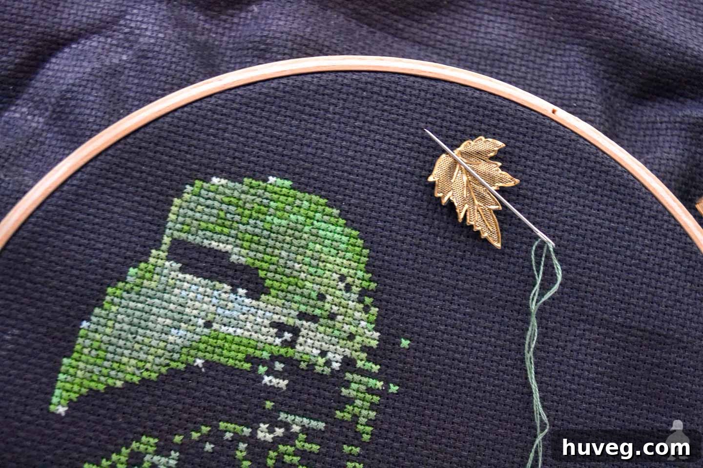 Gold leaf needle minder made from a repurposed jewelry charm.