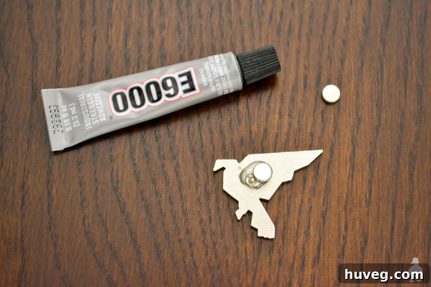 The magnet securely glued to the back of the enameled pin, curing on a wood background.