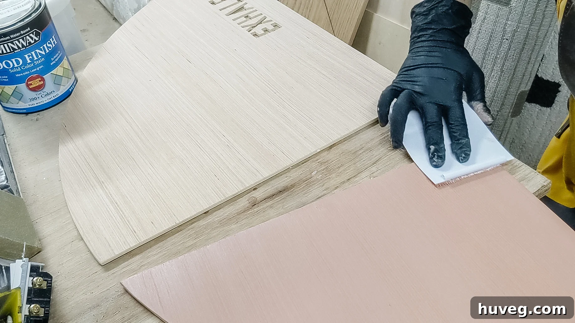 Applying Minwax solid color stain to the wood surface and wiping off excess for an even finish