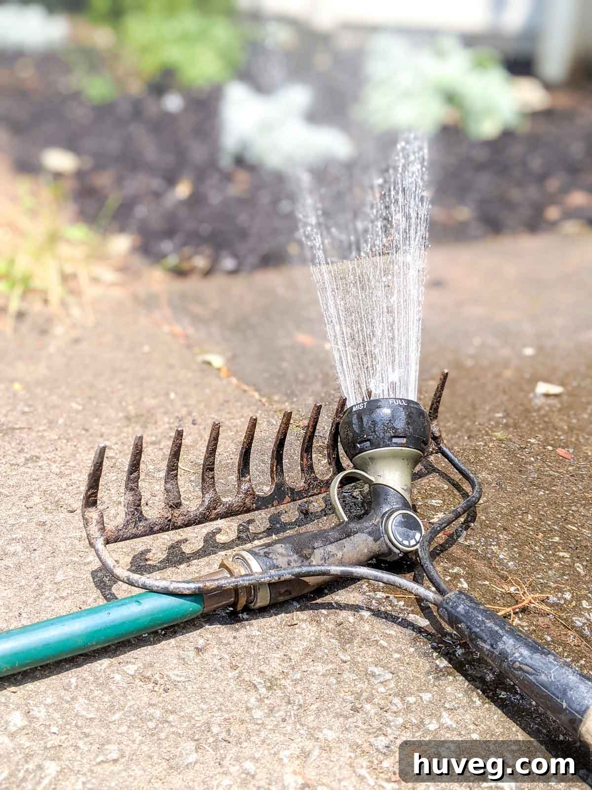 water hose propped up on a rake to turn into a sprinkler for the garden bed