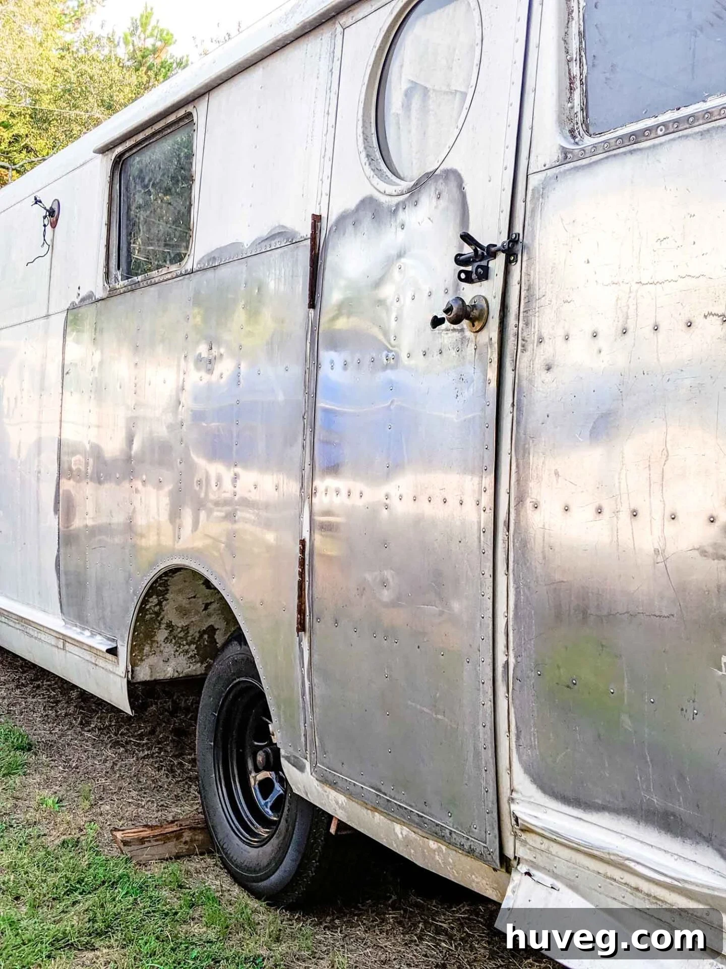 A glistening side panel of the Ruby vintage camper after initial aluminum polish, vividly reflecting its surroundings and showcasing remarkable improvement.