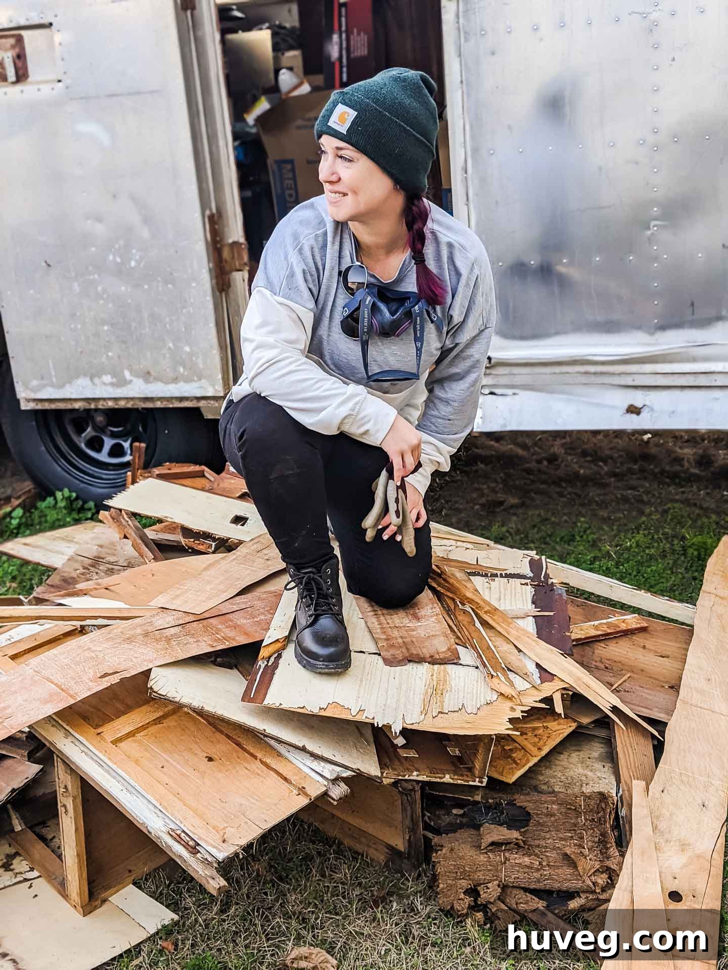 Woman sitting proudly on a large pile of removed interior demo materials from the Ruby camper restoration, amidst the significant progress.