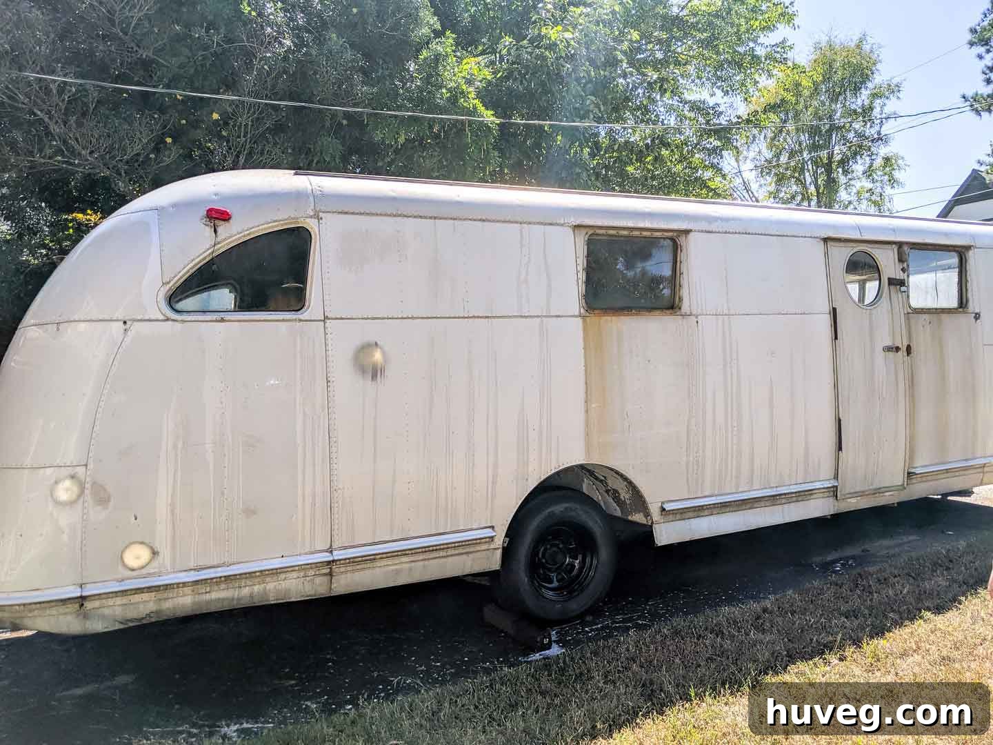 The vintage Spartan Manor camper exterior covered in heavy oxidation and grime after pressure washing, revealing years of neglect before polishing.