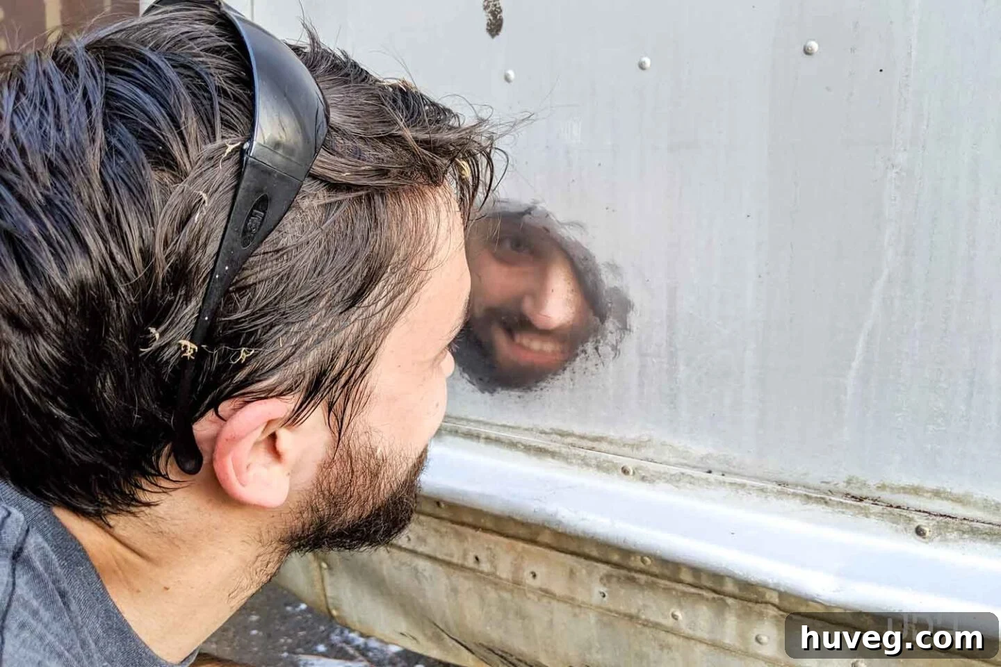 Kyle smiling joyfully as he clearly sees his reflection in the newly polished aluminum panel of the Ruby vintage camper, highlighting the surprising success of the polish.