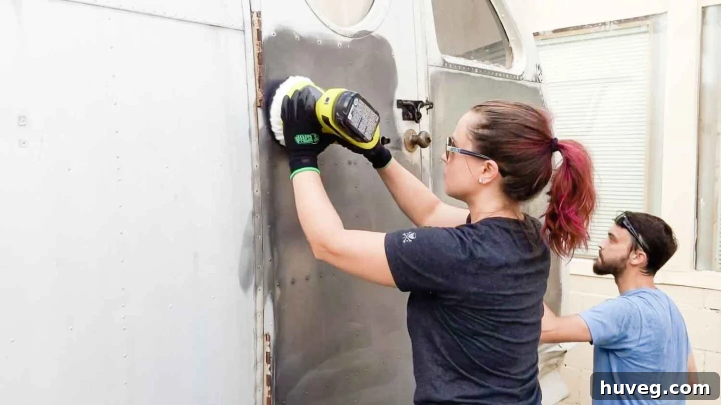 Team members polishing the vintage Ruby camper using battery-powered orbital buffer tools, with visible black residue indicating active oxidation removal.