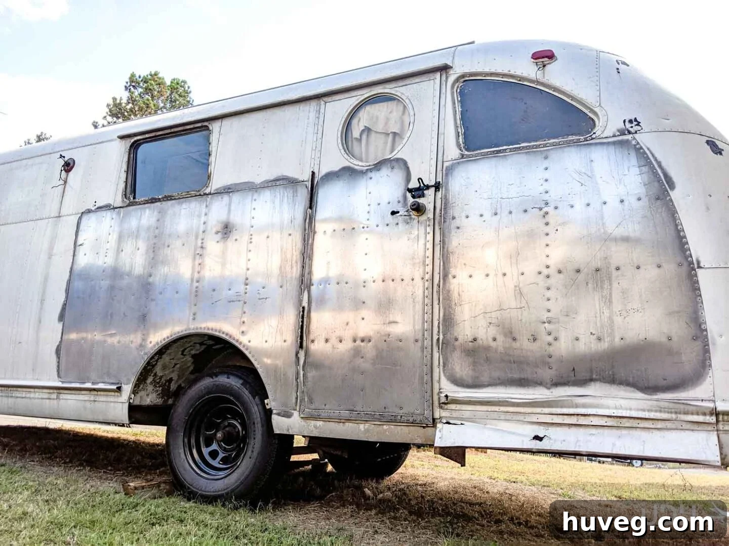 A section of the Ruby vintage camper's aluminum side shining brightly after the first polishing, showing a clear, surprising reflection of its surroundings.