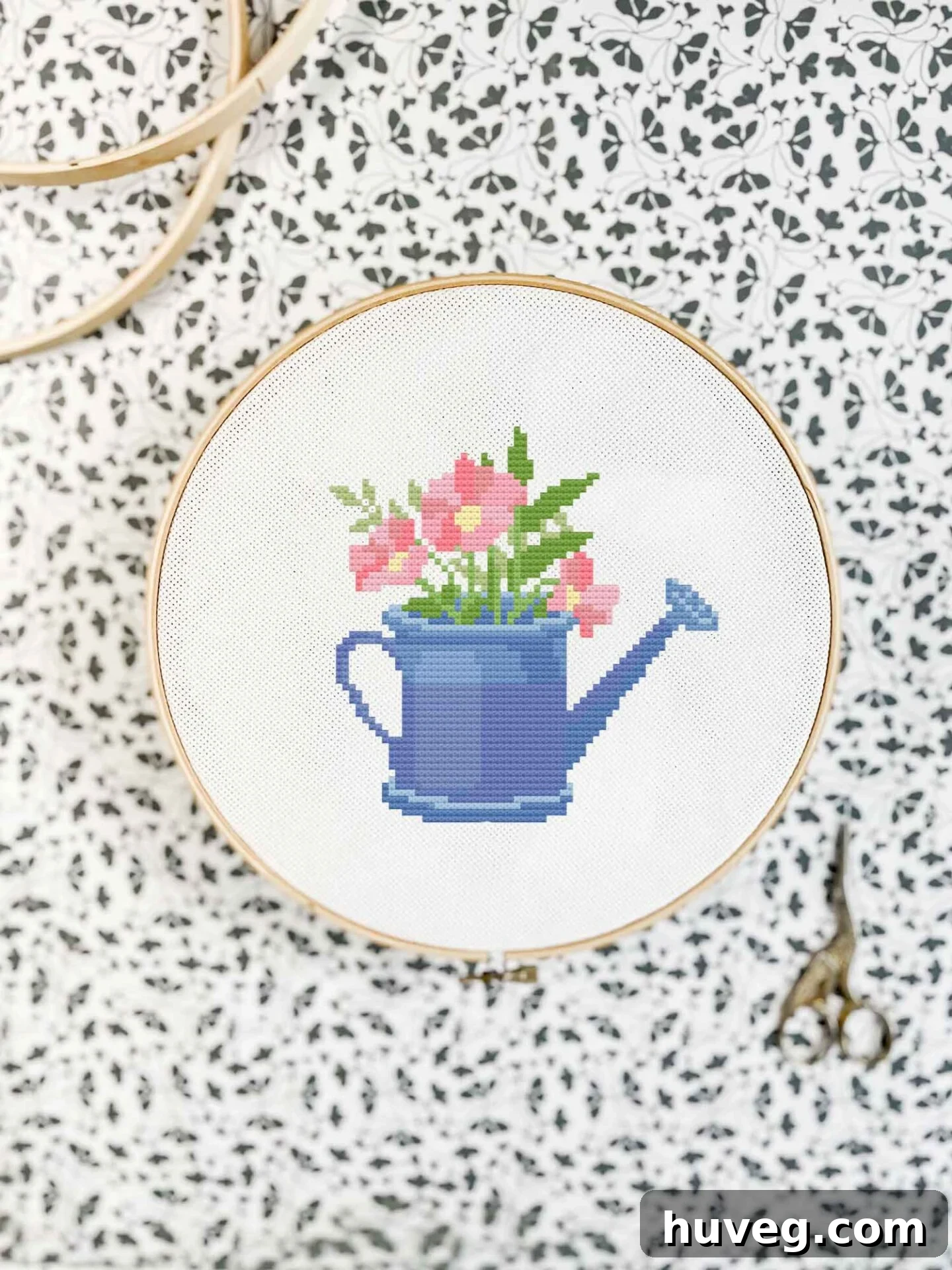 Close-up detail of the May Flowers cross stitch pattern showcasing a blue watering can and various pink, purple, and white flowers