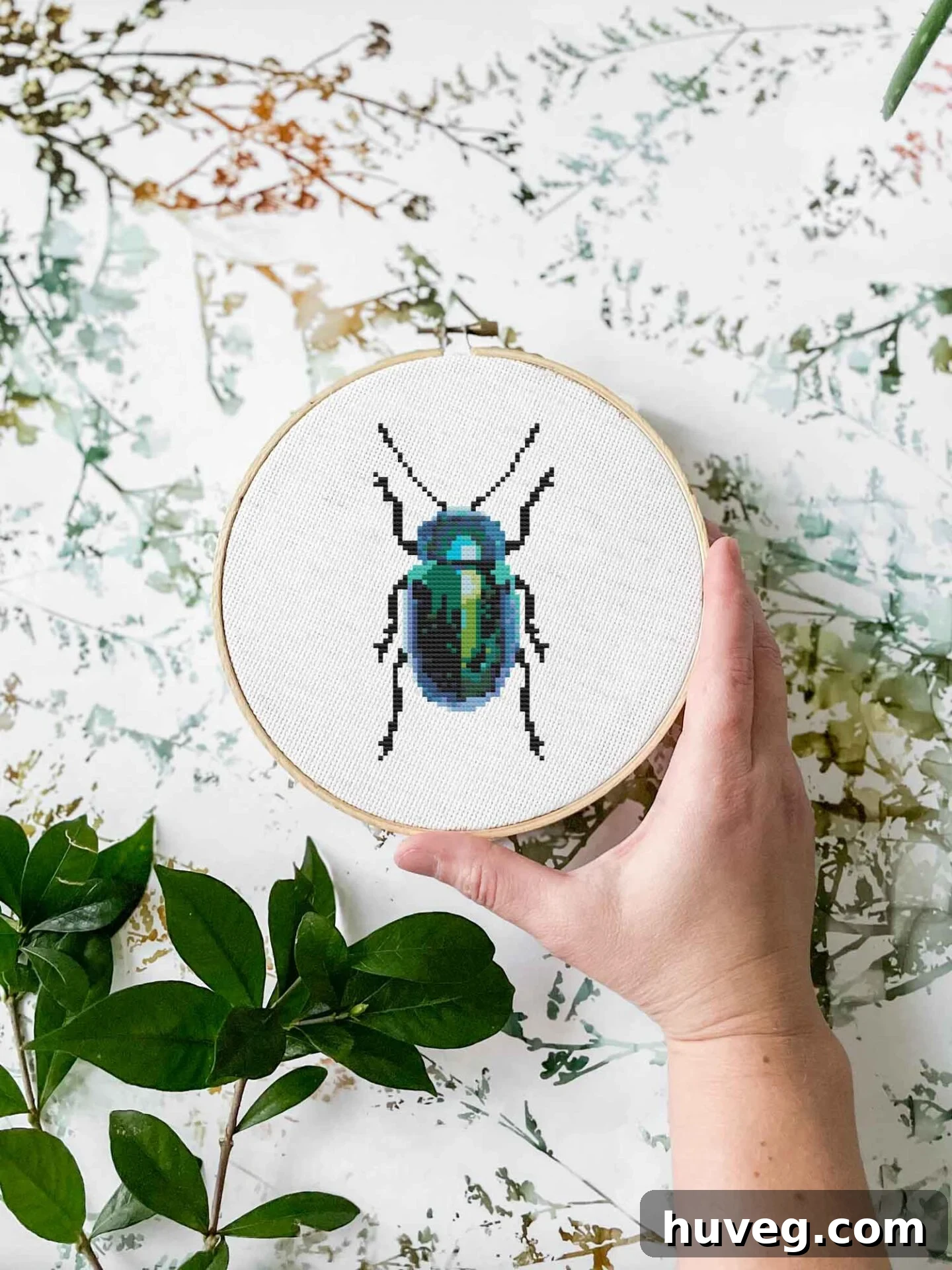 Close-up of the intricate Beetle Cross Stitch design, showcasing vibrant teal and green colors on fabric.