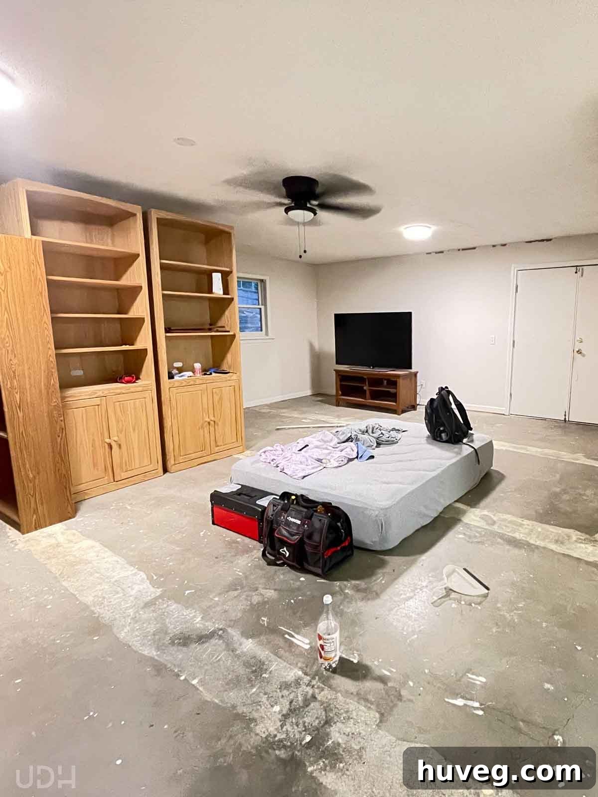 Basement living space before renovation with bare concrete floor and old stored furniture