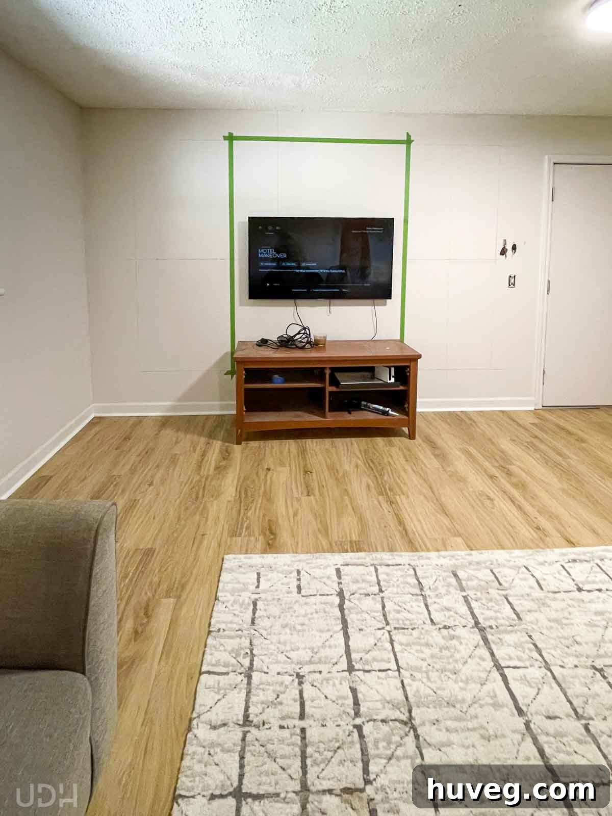 TV wall area in progress with new LVP flooring and a cozy rug. Green painter's tape maps out the new media wall project.